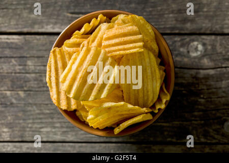 Crinkle cut potato chips on kitchen table. Tasty spicy potato chips in bowl. Top view. Stock Photo