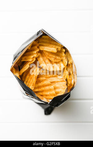 Crinkle cut potato chips on white table. Tasty spicy potato chips in bag. Top view. Stock Photo