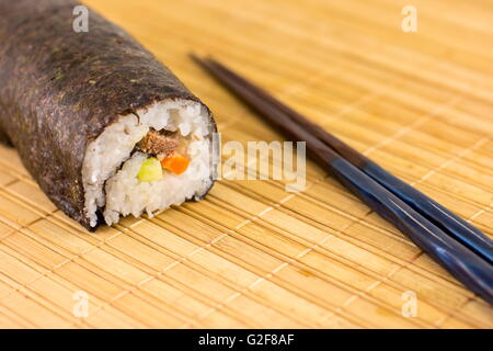 Sushi roll and chopsticks on bamboo tablecloth Stock Photo