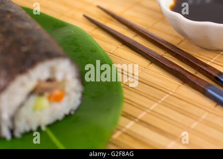 Sushi roll and chopsticks on bamboo tablecloth Stock Photo