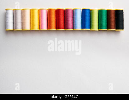 Spools of thread aligned on white cloth. Horizontal composition. Top view Stock Photo