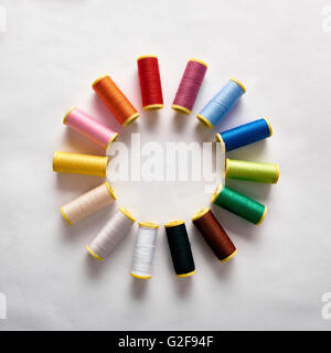 Spools of thread in circle on white cloth. Square composition. Top view Stock Photo