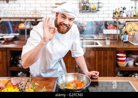 Smiling handsome chef cook preparing food and showing ok gesture on the kitchen Stock Photo