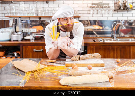 Funny bearded baker making moustache using macarons and working on the kitchen Stock Photo