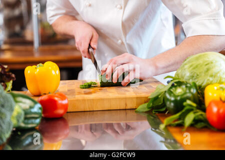 Closeup of green fresh cucumber cut by hands of professional chef cook on the kitchen Stock Photo