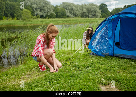 smiling friends setting up tent outdoors Stock Photo