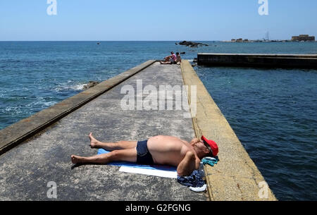 A  man lies alone, sunbathing beside the sea water swimming pool on the Paphos, seafront, Cyprus, Stock Photo