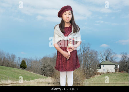 Portrait of Young Girl Holding Doll with Farm in Background Stock Photo