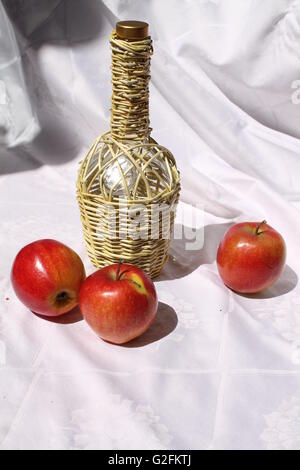 glass bottle into weave carcass with three red juicy apples nice decoration for dessert time Stock Photo