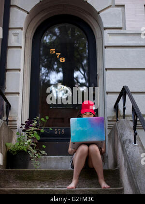 kid on front stoop working on laptop computer Stock Photo