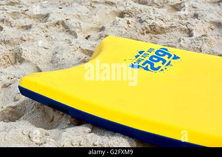 A yellow boogie board laying in the sand on the beach Stock Photo