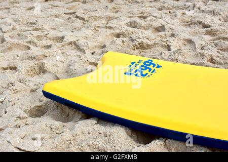 A yellow boogie board laying in the sand on the beach Stock Photo