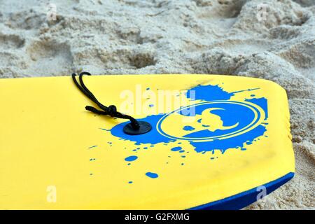 A yellow boogie board laying in the sand on the beach Stock Photo