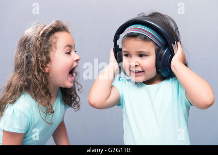 Portrait of black-haired girl in headphones with older sister screaming Stock Photo