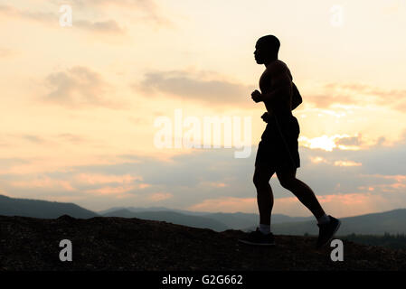 Silhouette of african american athlete jogging on sunset in mountains. Training outdoor Stock Photo