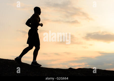 Silhouette of african american athlete man jogging on sunset in mountains. Training outdoor. Sport and fitness concept Stock Photo