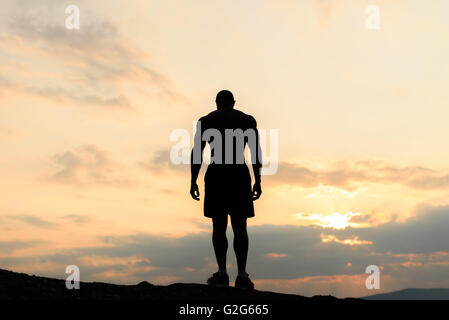 Back view on silhouette of bodybuilder posing at the sunrise or sunset in mountains. Handsome strong man showing his muscles Stock Photo