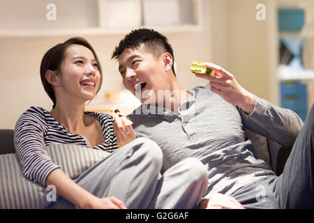 Happy young couple eating cakes on sofa Stock Photo