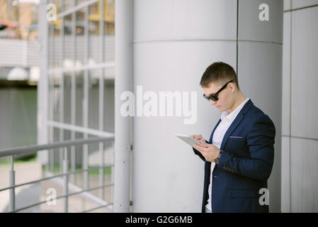 Portrait of a young businessman seeing on his tablet pc on the street. Man in blue suit with dark sunglasses. Stock Photo
