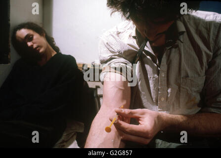 A heroin addict shooting up while his girliend is already high. Stock Photo