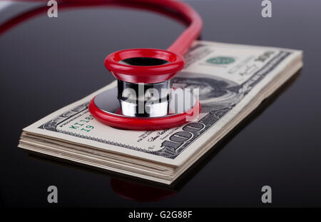 Red stethoscope on a pile of dollars closeup reflected on black  background Stock Photo