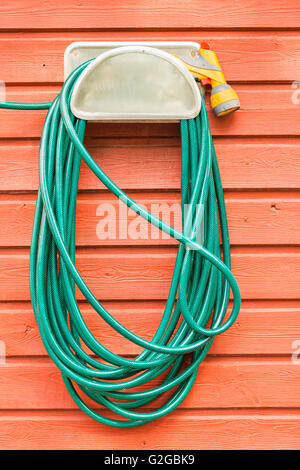 Green plastic garden hose and nozzle hanging on the wall of a red wooden house, Stockholm, Stockholm County, Sweden Stock Photo