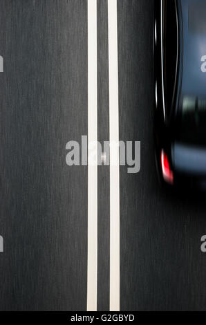 double white lines divider on blacktop with a car passing Stock Photo