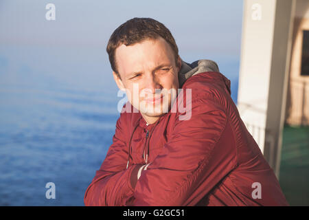 Young handsome Caucasian man standing on the walking deck of cruise ship in bright evening sunlight Stock Photo