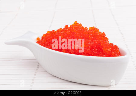 Red caviar in a fish shape bowl on white wooden background Stock Photo