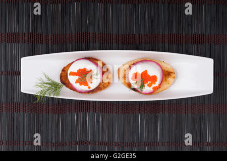 Two roasted breads with radish cheese and red caviar on long white plate on dark wood background Stock Photo