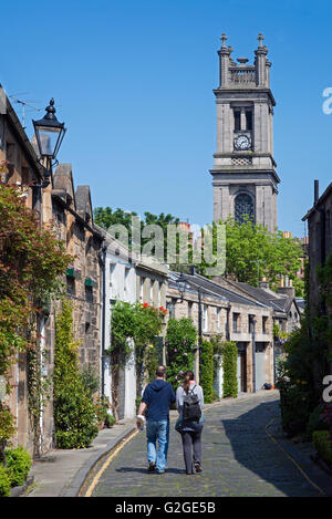 A couple stroll along Circus Lane with the tower of St Stephen's Church in the background - Stockbridge, Edinburgh. Stock Photo