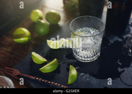 Close up shot of fresh drink with lemons on a bar counter. Glass filled with cocktail and lemon slices on the board with spoon. Stock Photo