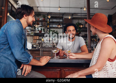 Three young friends smiling and sitting in a cafe having drinks together. Young modern people sitting in the coffee shop and hav Stock Photo