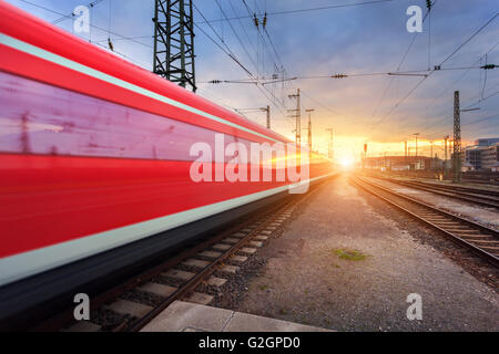 High speed red passenger train on railroad track in motion at sunset. Blurred commuter train. Railway station in Nuremberg Stock Photo