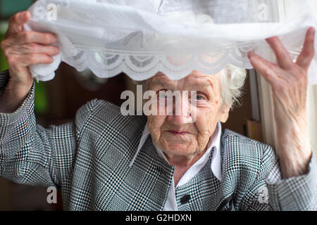 Elderly woman peeks out from behind the curtain. Stock Photo