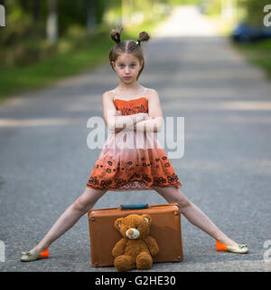 Little girl traveler with suitcase and Teddy bear is on the road. Stock Photo