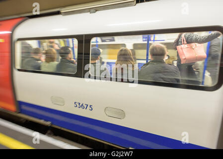 People sitting on a London Underground Tube train traveling to their destinations with blurred movement of the train in action Stock Photo