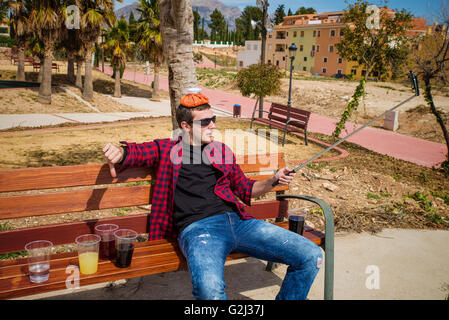 Guy documenting his hangover on a park bench with a selfie, a concept Stock Photo