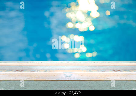 Perspective wood table top and Soft focus bokeh light effects over a rippled, blue water background in the pool, product display Stock Photo