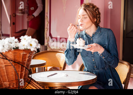 Relaxed pretty young woman sitting and eating cupcake in outdoor cafe Stock Photo