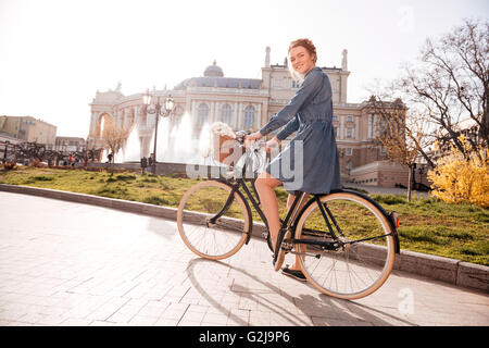 Happy pretty young woman riding a bike near the theatre Stock Photo