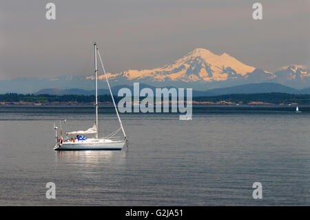 A sailboat off Willows Beach in Oak Bay in Victoria, British Columbia.  In the background is Mt. Baker in Washington State, USA. Stock Photo