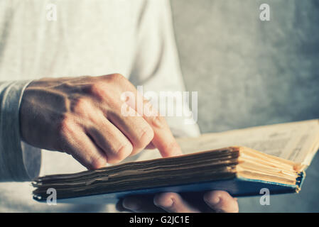 Man reading old book with torn pages, close up of adult male hands holding vintage book. Stock Photo