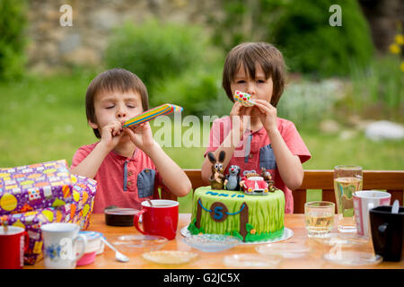 Beautiful adorable five year old boy, celebrating his birthday, blowing candles and eating the cake, outdoors. Birthday party fo Stock Photo