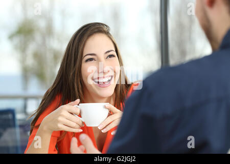 Happy woman dating in a coffee shop looking at her partner and holding a cup Stock Photo