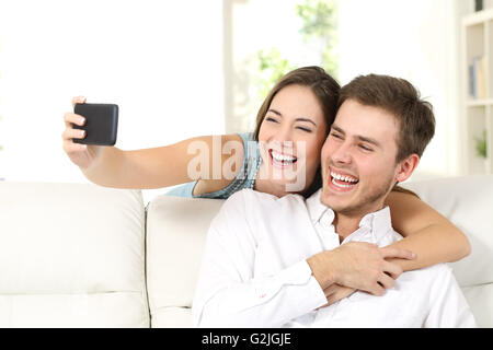 Marriage or couple laughing and taking a selfie with phone sitting on a couch at home Stock Photo