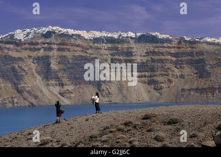 Tourists taken photos of Oia resort from Kameni volcanic islet, in Santorini island, Cyclades, Greece Stock Photo