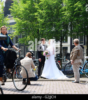 Best man looks on as newly married couple pose for photograph on Amsterdam bridge.  Lady cycles past scene. Stock Photo