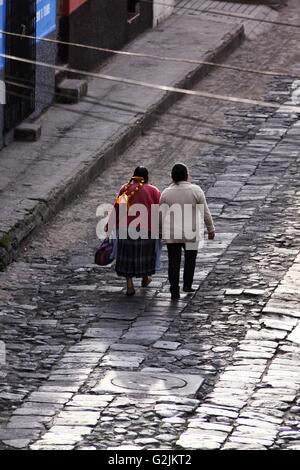 A Mayan Guatemalan mother and grandmother walk down a wet reflective cobblestone street in Quetzaltenango Stock Photo