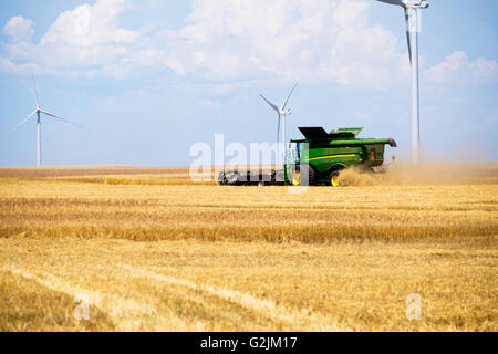 A John Deere combine harvests wheat in Oklahoma, USA.Wind farm in background.